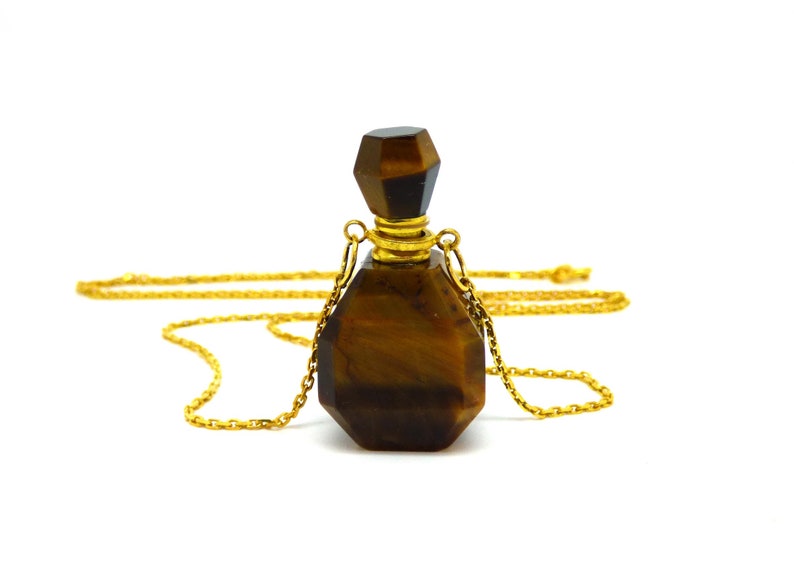 Puede incluir: Un collar de cadena dorada con un colgante de botella de piedra de ojo de tigre. La botella es facetada y tiene una tapa dorada.