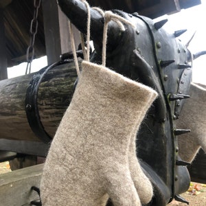 May include: A pair of beige wool mittens with a string loop hanging from a metal object.