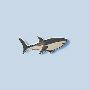 May include: A cartoon-style illustration of a shark. The shark has a white underbelly, a grey back, and black fins. It is set against a light blue background. The design is simple and could be used for various purposes.