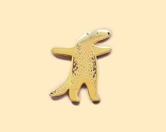 May include: A gold-coloured metal pin shaped like an anteater standing on its hind legs with its front legs outstretched. The anteater has a long snout and a textured body.