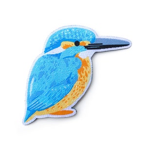 May include: An embroidered patch of a kingfisher bird, featuring blue and orange colours.