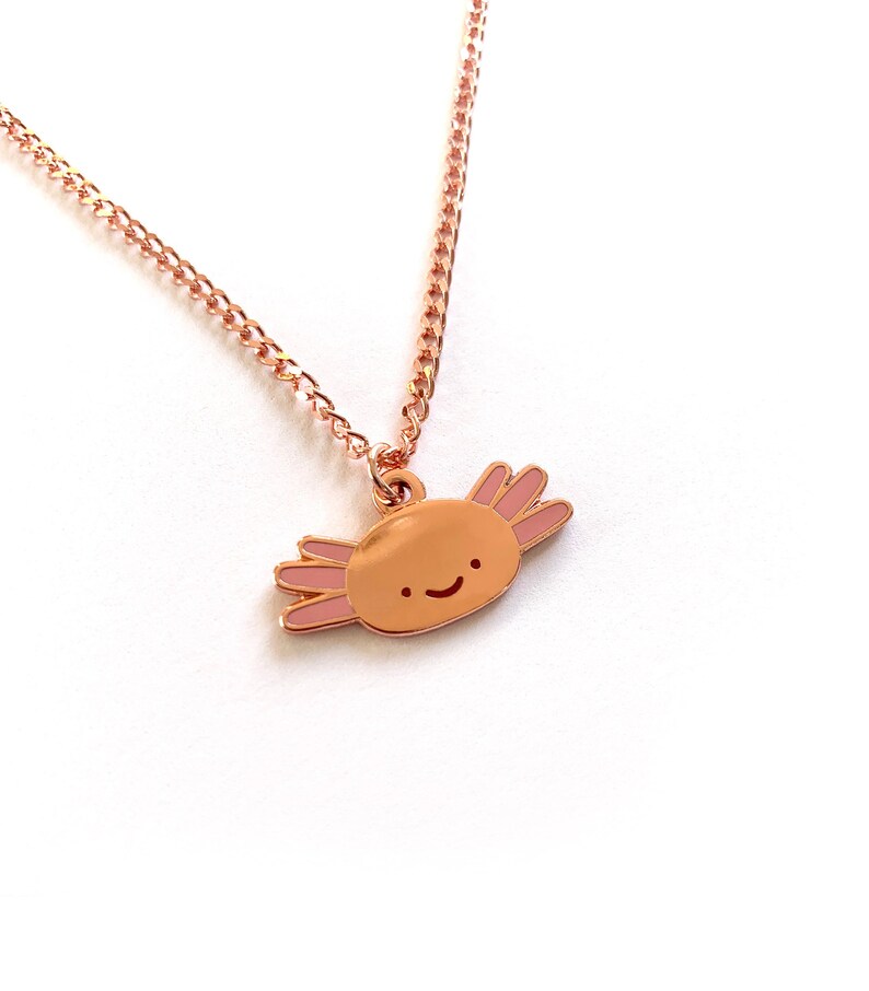 May include: A rose gold necklace featuring a charming axolotl charm. The axolotl is smiling and has pink gills.