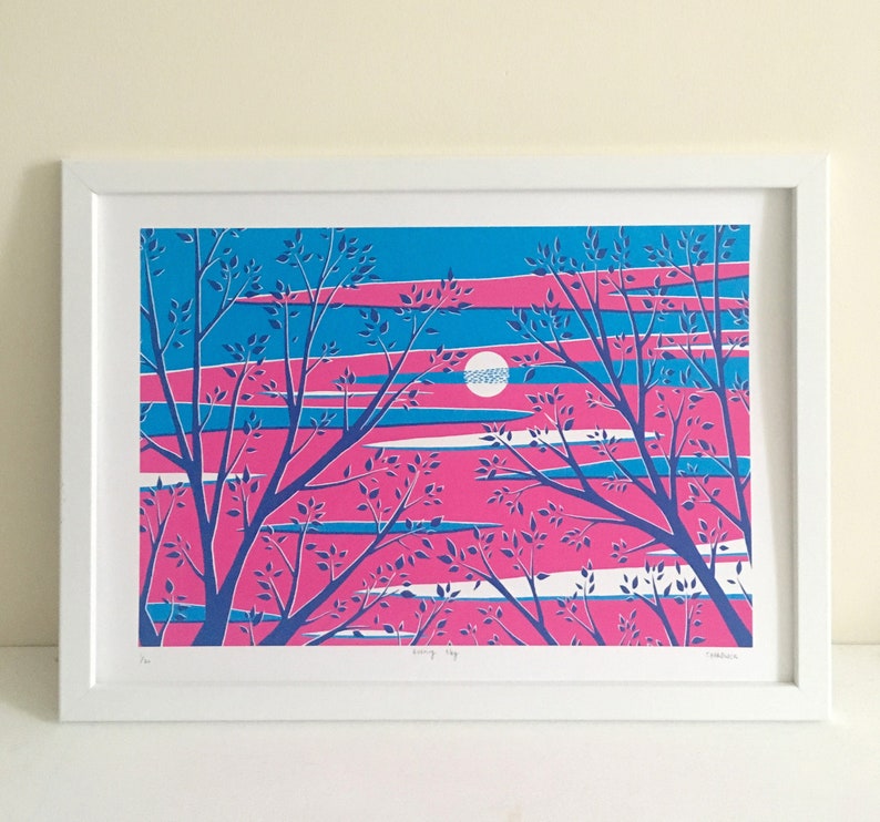 May include: A framed art print featuring a stylized landscape. The artwork showcases a vibrant color palette of pink, blue, and white, depicting a sunset or sunrise scene with silhouetted trees. The print is in a white frame.