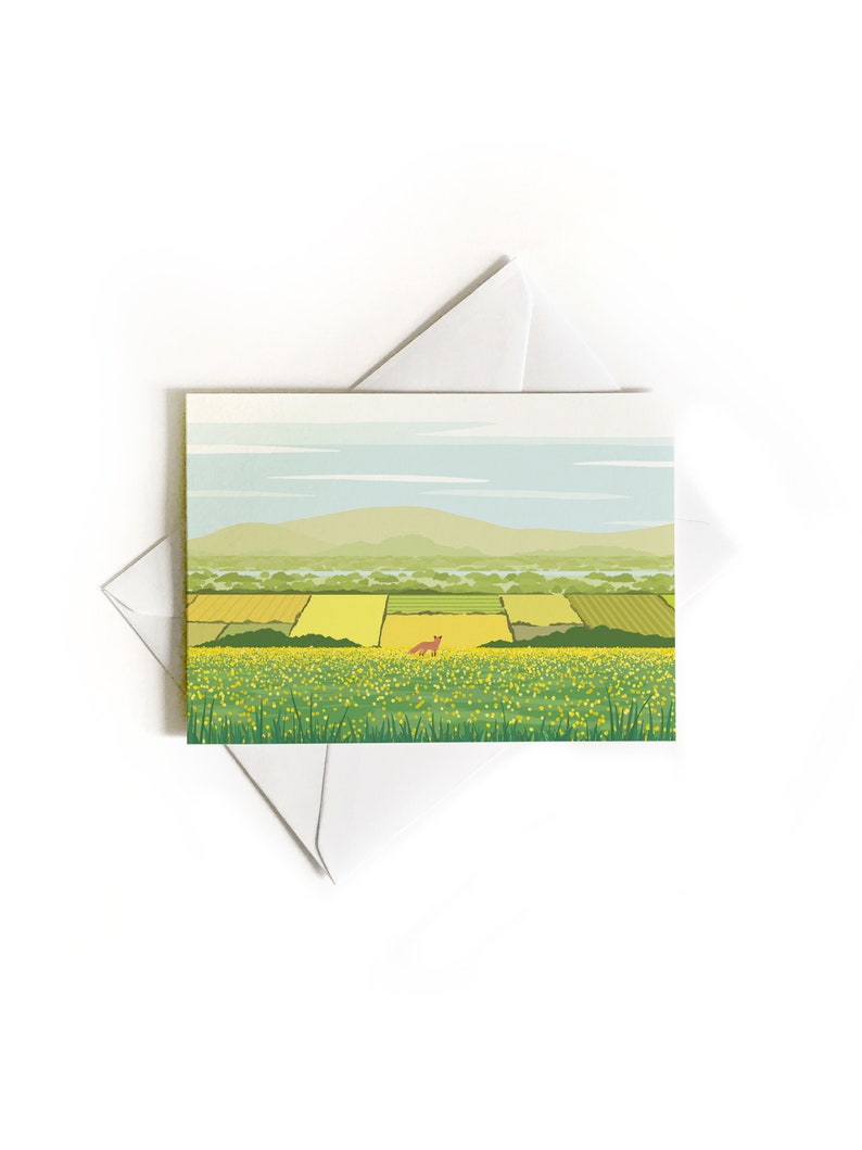 May include: A green field with yellow flowers and a red fox in the distance. The field is surrounded by green trees and a blue sky with white clouds. In the background, there are mountains.