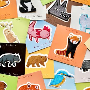 Könnte beinhalten: Eine Sammlung von gestickten und gewebten Aufbügel-Patches mit verschiedenen Tiermotiven, darunter ein Panda, Wolf, Faultier, Axolotl, roter Panda, Bär und Eisvogel, jeweils auf quadratischen Karten mit der Aufschrift Tom Hardwick.