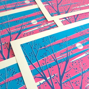 May include: A collection of art prints featuring a stylized landscape. The prints showcase a vibrant color palette of pink, blue, and white. The design includes silhouetted trees and a moon, set against a backdrop of diagonal stripes.