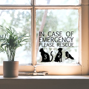 Op de afbeelding: Een raamsticker met de tekst "IN GEVAL VAN NOOD REDDEN" en drie zwarte silhouetten van dieren: een kat, een hond en een vogel. De dieren zijn genummerd 3, 2 en 1.