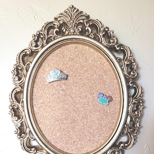 Tablero de corcho con marco y alfileres dorados ornamentados para intercambio.