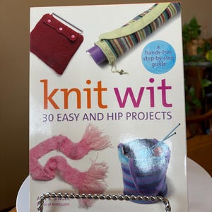 Może przedstawiać: Książka zatytułowana "knit wit" z podtytułem "30 łatwych i modnych projektów" jest prezentowana w metalowym stojaku. Okładka zawiera zdjęcia dzianin, w tym czerwoną torebkę, pasiasty futerał i różowy szalik. Książka jest przewodnikiem krok po kroku.