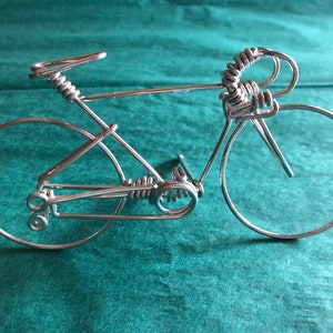 May include: A silver wire sculpture of a bicycle with a coiled handlebar and a detailed chain.