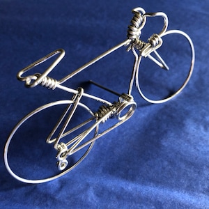 May include: A silver wire sculpture of a bicycle with a detailed design. The sculpture is on a blue background.