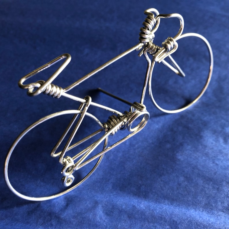 May include: A silver wire sculpture of a bicycle with a detailed design. The sculpture is on a blue background.