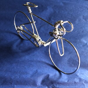May include: A silver wire sculpture of a bicycle. The sculpture is made of twisted wire and has a realistic design.