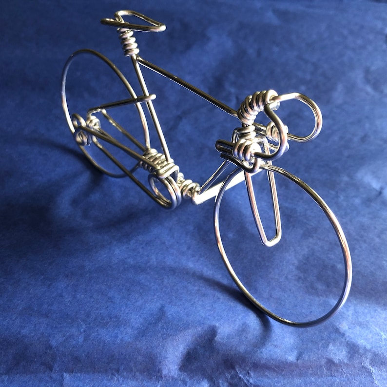 May include: A silver wire sculpture of a bicycle. The sculpture is made of twisted wire and has a realistic design.