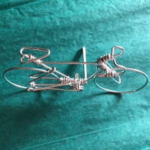 May include: A silver wire sculpture of a bicycle. The sculpture is made of twisted wire and has a simple, minimalist design.