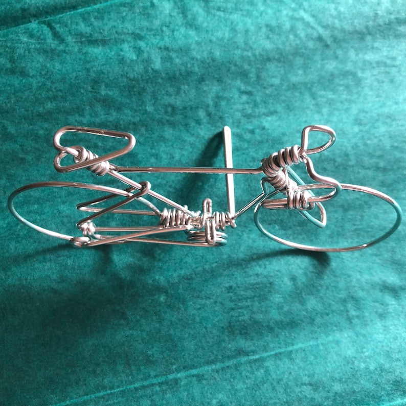 May include: A silver wire sculpture of a bicycle. The sculpture is made of twisted wire and has a simple, minimalist design.