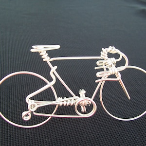 May include: A silver wire sculpture of a bicycle with a detailed design. The sculpture is made of thin wire and has a realistic shape.