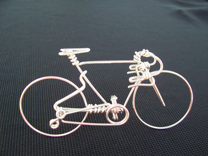 May include: A silver wire sculpture of a bicycle with a detailed design. The sculpture is made of thin wire and has a realistic shape.