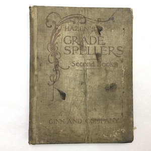May include: An antique book titled "Hazen's Grade Spellers Second Book" with a faded, textured cover. The cover is a muted olive green with brown lettering and decorative flourishes. The publisher's name, Ginn and Company, is printed at the bottom.