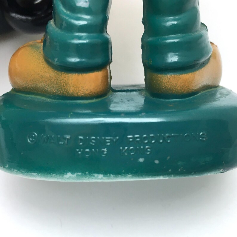Op de afbeelding: Een close-up van een vintage beeldjevoet. De voet is zeegroen met de tekst "&copy; WALT DISNEY PRODUCTIONS HONG KONG" in het wit. De benen van het beeldje zijn zeegroen en de schoenen zijn goud.