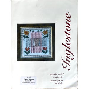 May include: A framed cross-stitch pattern titled "Darned Buttons Lattice Pot." The design features a central pot motif surrounded by floral elements in shades of red, yellow, and green. The finished piece measures 4.5 inches square.