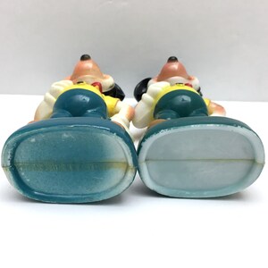 Op de afbeelding: Twee vintage Goofy-beeldjes, van achteren bekeken, tonen hun onderscheidende kenmerken. Elke figuur heeft een lichtbruin hoofd, zwarte oren en een geel shirt met een blauwe overall. De basis is lichtblauw.