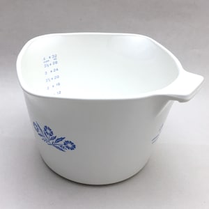 May include: A white ceramic mug with a black handle and the text "But First, Coffee" in a bold, black font. The mug is set against a blurred background, suggesting a cozy setting. The mug appears to be approximately 4 inches tall.