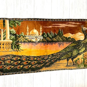 May include: A decorative tapestry featuring a peacock with a long, detailed tail. The background depicts a landscape with a mosque, trees, and a body of water. The color palette includes shades of green, brown, and gold.