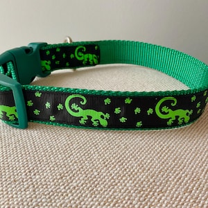 May include: A green and black dog collar with a green lizard pattern. The collar has a green buckle and is made of nylon.