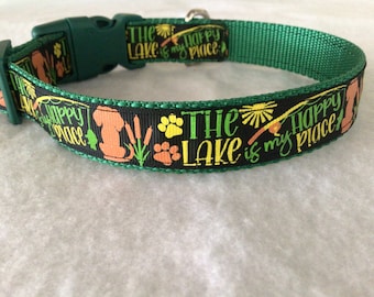 Puede incluir: Collar de perro verde con cinta negra con el texto "The Lake is my happy place" con una caña de pescar, huellas de patas y una silueta de perro.