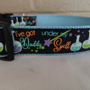 May include: Black and blue dog collar with a white, green, and purple print of potion bottles, stars, and the text "I've got Daddy under my spell".
