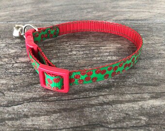 May include: Red and green cat collar with a bell. The collar has a red buckle and a green ribbon with red polka dots.