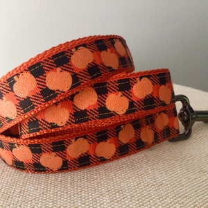 May include: Orange and black plaid ribbon with orange pumpkin designs. The ribbon is folded and has a metal clasp attached, perfect for a seasonal craft project or pet accessory.