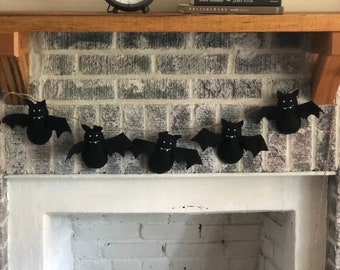 May include: A white brick fireplace mantel with a black clock, a stack of books, and a black bat garland hanging above the fireplace.