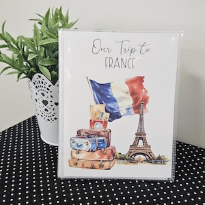 May include: A white card with the text "Our Trip to France" and a watercolor illustration of the Eiffel Tower, suitcases, and a French flag.