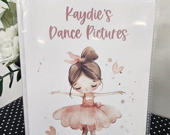 Peut inclure: Un album photo blanc avec une couverture en plastique transparent. Le devant de l'album présente une illustration aquarelle d'une ballerine vêtue de rose et de marron. Le texte "Kaydie's Dance Pictures" est imprimé en rose sur le devant de l'album.