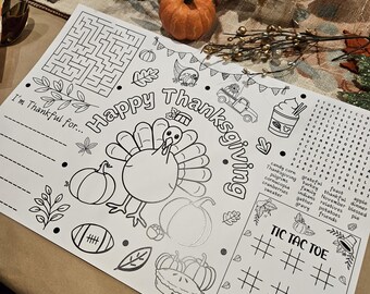 May include: Thanksgiving-themed activity placemat with a turkey illustration, pumpkins, and the words "Happy Thanksgiving." Includes a maze, word search, and Tic-Tac-Toe game. An orange pumpkin sits nearby.