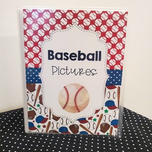 Peut inclure: Un classeur en plastique transparent avec un motif sur le th&egrave;me du baseball rouge, blanc et bleu. La couverture avant pr&eacute;sente un ballon de baseball avec des coutures, des battes, des gants et des casquettes. Le titre "Baseball Pictures" est imprim&eacute; en noir sur fond blanc.