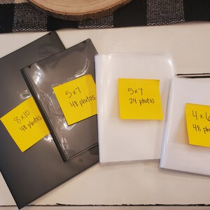 Peut inclure: Quatre albums photos de tailles diff&eacute;rentes. Deux sont noirs avec des notes autocollantes jaunes indiquant "8x10 48 photos" et "5x7 48 photos". Deux sont blancs avec des notes autocollantes jaunes indiquant "5x7 24 photos" et "4x6 48 photos".