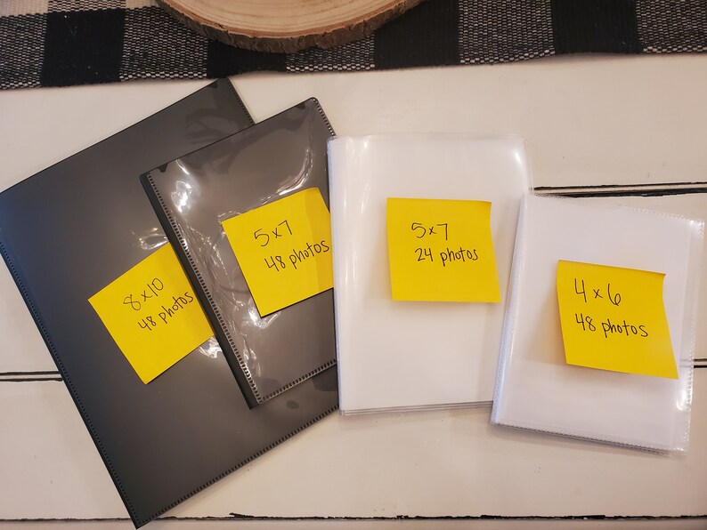 Peut inclure: Quatre albums photos de tailles diff&eacute;rentes. Deux sont noirs avec des notes autocollantes jaunes indiquant "8x10 48 photos" et "5x7 48 photos". Deux sont blancs avec des notes autocollantes jaunes indiquant "5x7 24 photos" et "4x6 48 photos".