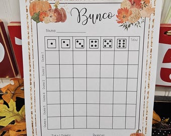 May include: A printed Bunco score sheet with a fall theme. The sheet features the word "Bunco" in cursive, along with illustrations of pumpkins and flowers. It includes spaces for names, dice rolls, and game scores. The sheet is bordered with a gold design.