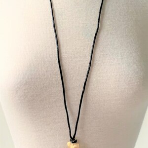 May include: A gold cross pendant necklace with a red gemstone in the center, hanging from a black cord.