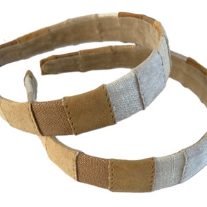 May include: Two brown and beige fabric headbands with a woven design. The headbands are made of a combination of suede and linen.