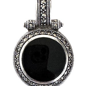 May include: A silver-toned pendant with a round, black onyx stone center. The pendant is framed with small, sparkling accents and has a decorative bail. The design is classic and elegant, suitable for various occasions.