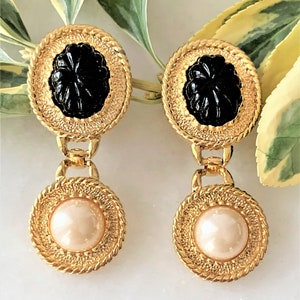 May include: Gold tone drop earrings with black and white cameo-style stones. The top portion of the earrings features a black stone with a raised design, while the bottom portion features a white pearl-like stone.