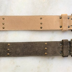 May include: Two suede belts with brass buckles and studs. The top belt is light brown and the bottom belt is dark green.