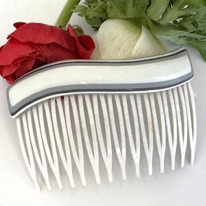 May include: A white plastic comb with a gray and white striped design. The comb is curved and has a rounded handle.