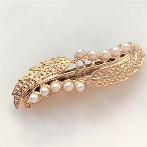 May include: A gold hair clip with a leaf design and pearl accents.