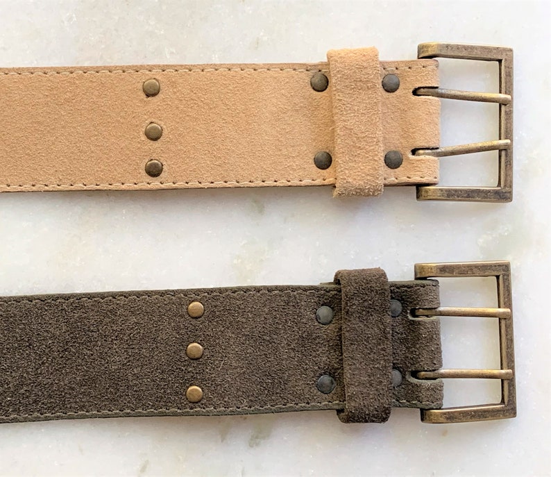 May include: Two suede belts with brass buckles and decorative studs. The top belt is light brown and the bottom belt is dark brown.