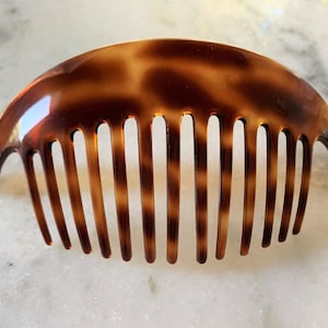 May include: A brown tortoiseshell plastic hair comb with a curved shape and a row of teeth.